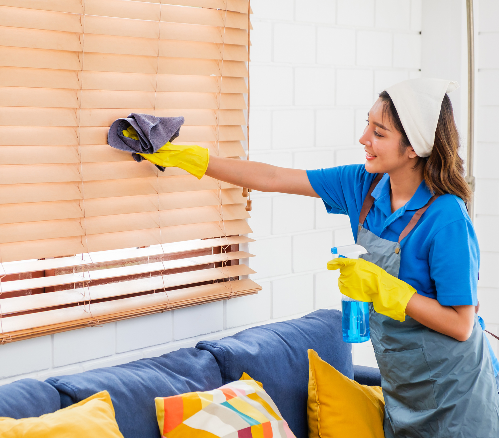 Housekeeper dusting blinds with yellow gloves